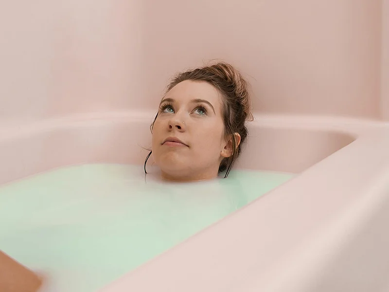 Woman laying in bubble bath with pink bath and walls